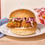 A fried chicken sandwich topped with slaw on a white plate.