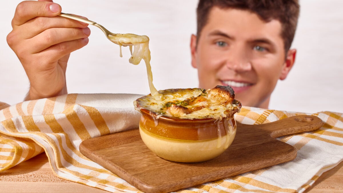 Nick DiGiovanni lifting a spoonful of soup from a bowl of French onion soup, creating a cheese pull. 