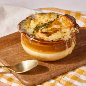 A bowl of classic French onion soup on a wooden cutting board with a spoon.