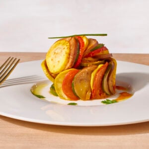 A serving of ratatouille on a plate topped with fresh herb.