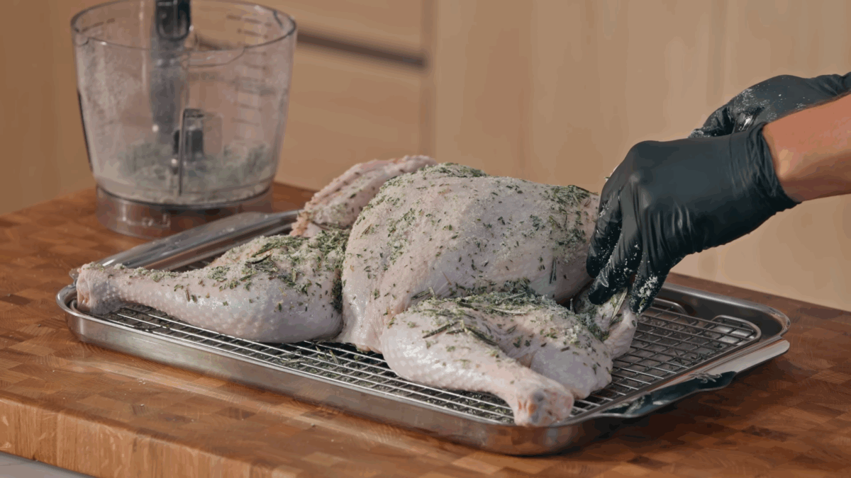 Nick DiGiovanni covering a raw spatchcocked Thanksgiving turkey with herbed salt. 