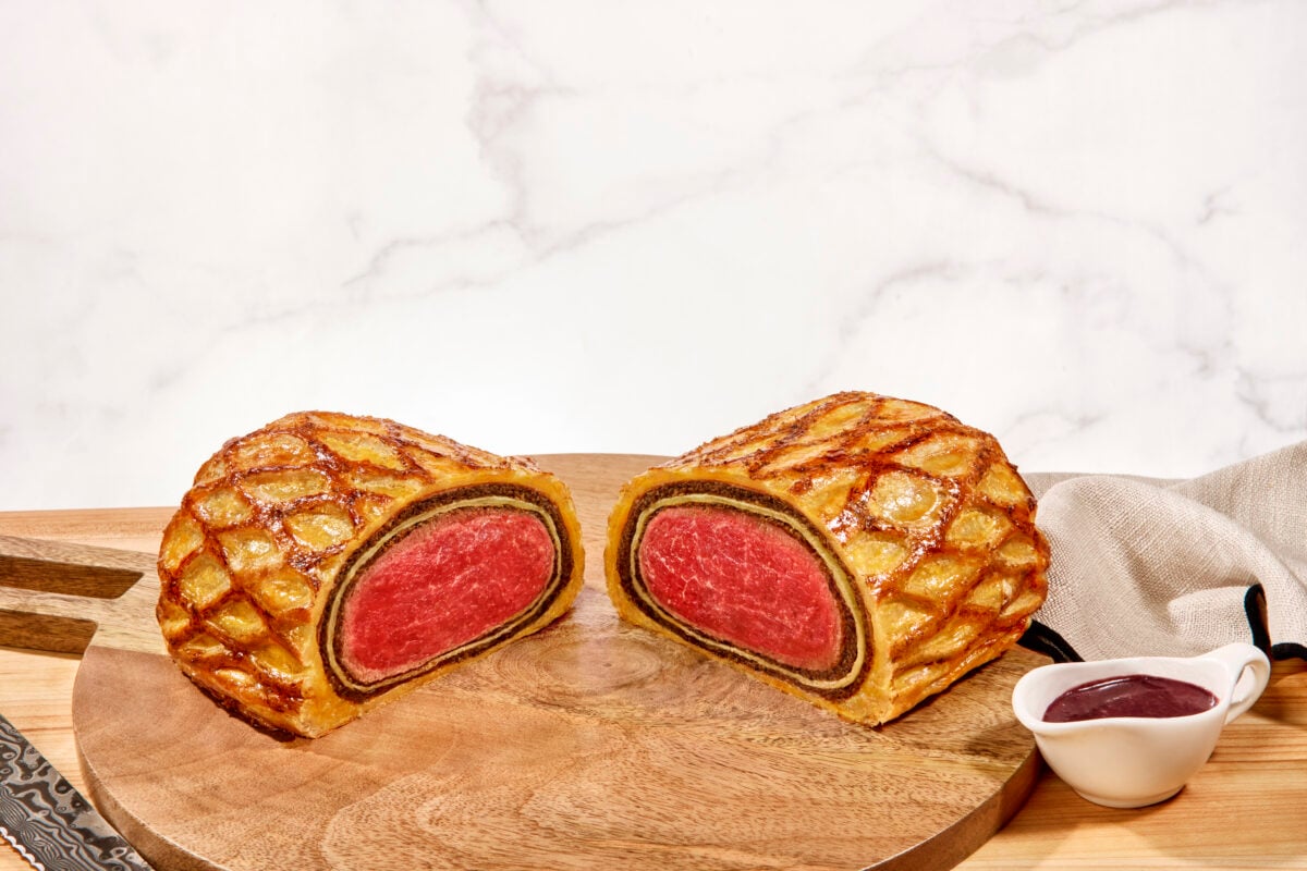 A Beef Wellington on a wooden cutting board, sliced in half. 