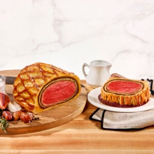 A Beef Wellington on a platter and a slice cut on a plate.
