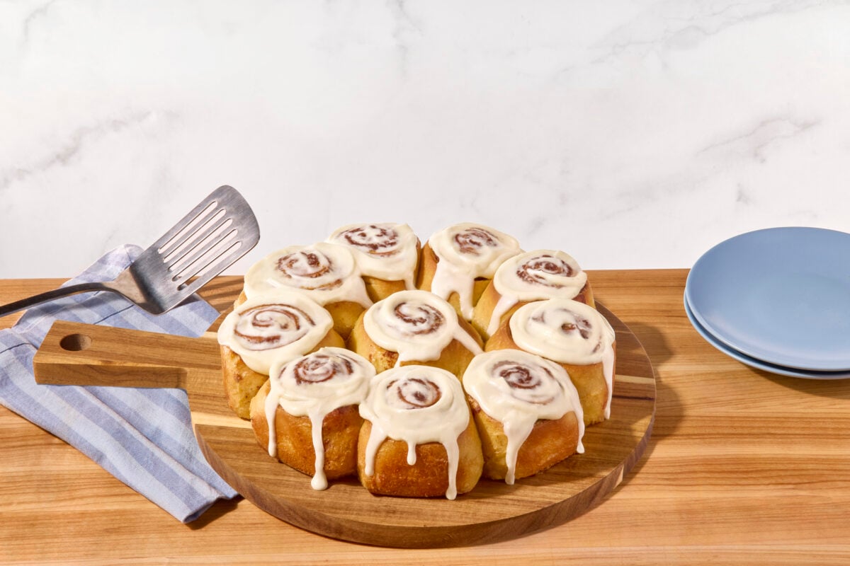 A batch of homemade cinnamon rolls on a wooden cutting board.  