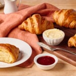 Homemade croissants on a wooden cutting board and one half of one on a plate.