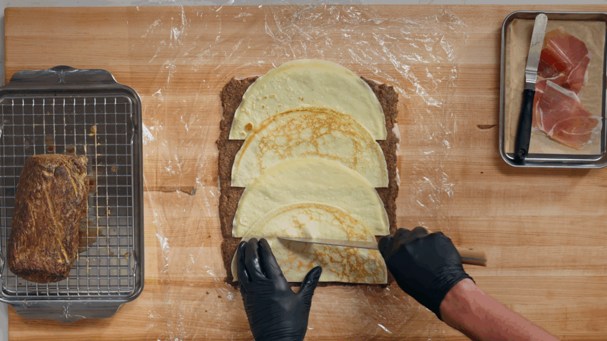 Nick DiGiovanni layering Beef Wellington ingredients on plastic wrap. 