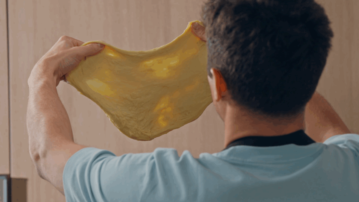 Nick DiGiovanni holding up cinnamon roll dough to reveal the window pane appearance.