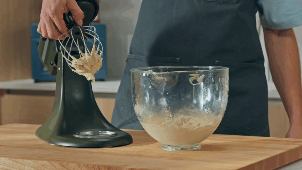 Nick DiGiovanni removing a whisk attachment covered in cinnamon roll filling from a stand mixer. 