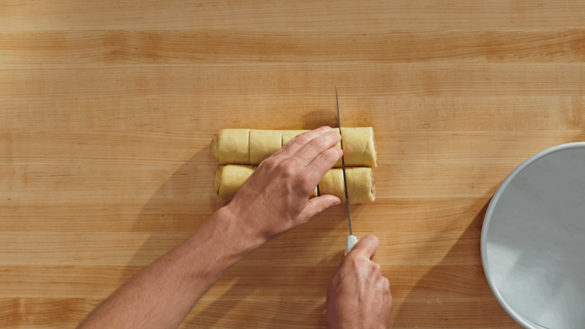 Nick DiGiovanni slicing raw cinnamon roll dough into ten pieces. 