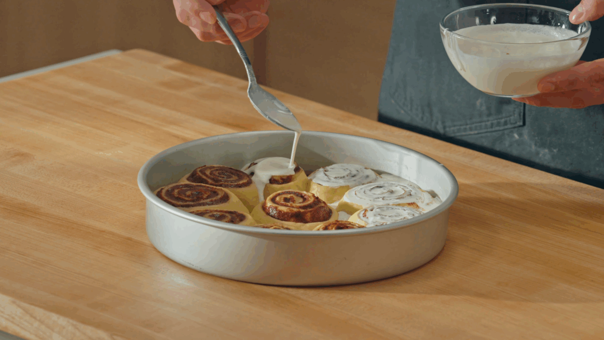 Nick DiGiovanni pouring heavy cream over cinnamon rolls in a round pan. 