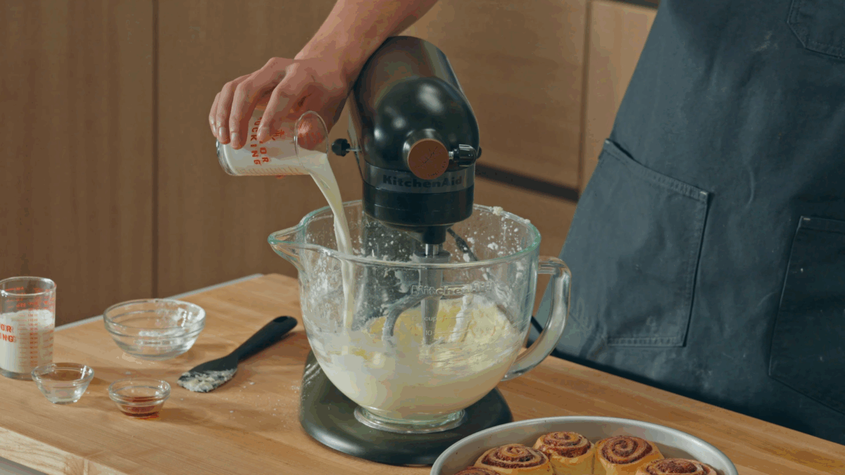 Nick DiGiovanni pouring milk into the bowl of a stand mixer with cream cheese frosting.  