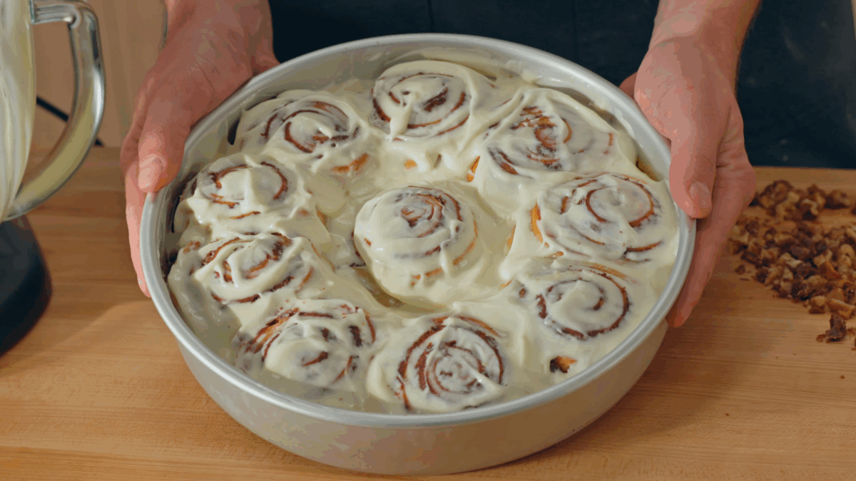 Nick DiGiovanni holding a cake pan of homemade cinnamon rolls topped with cream cheese frosting. 