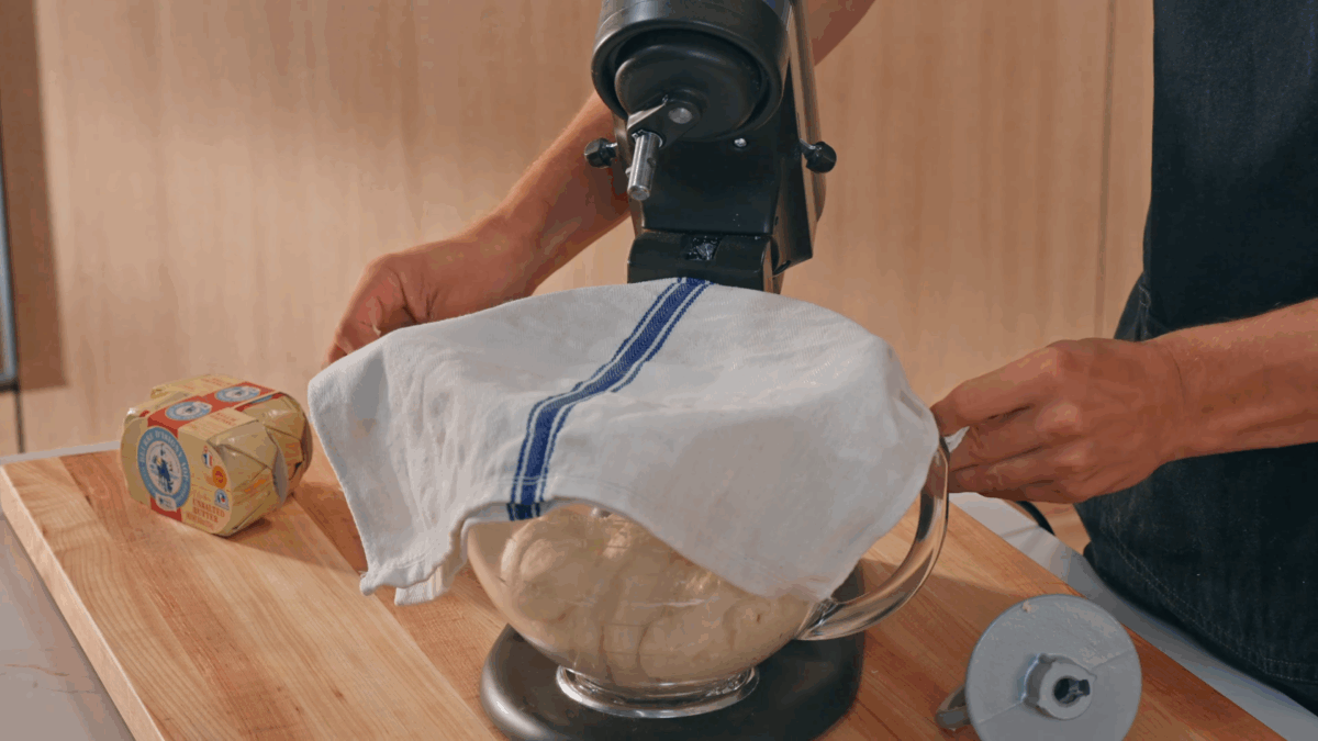 Nick DiGiovanni placing a tea towel over a bowl of croissant dough. 