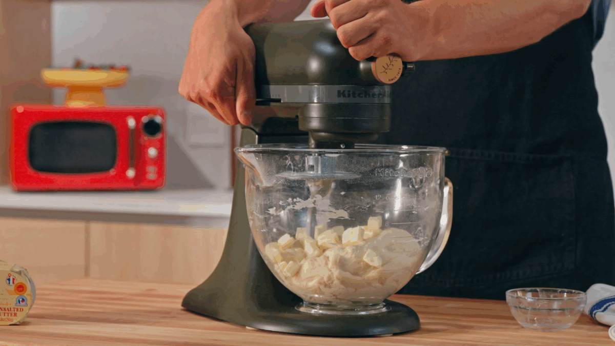 Nick DiGiovanni adding butter pieces to croissant dough in a stand mixer. 