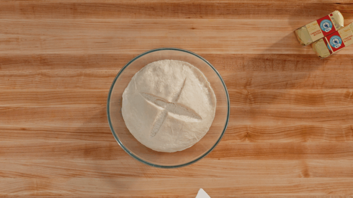 A ball of homemade croissant dough in a bowl with an "X" scored on top. 