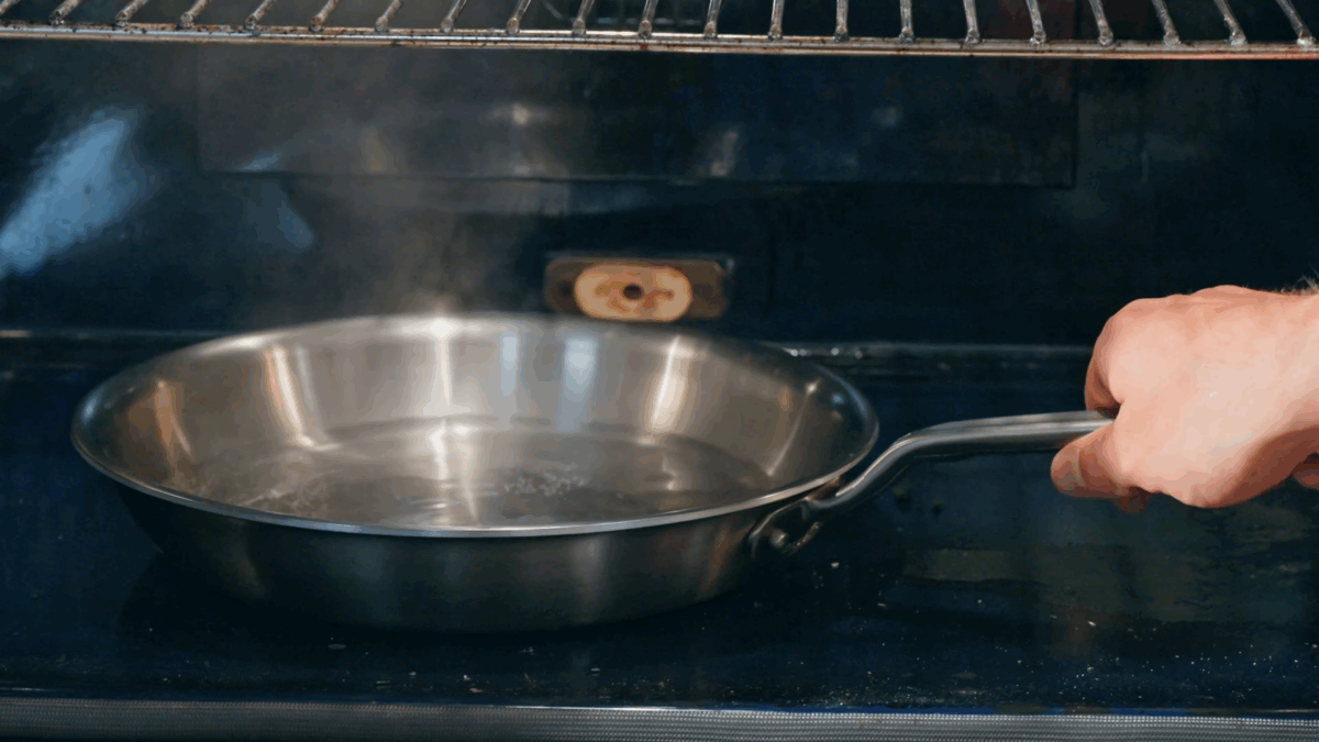 Nick DiGiovanni placing a skillet of steaming water on the floor of an oven. 