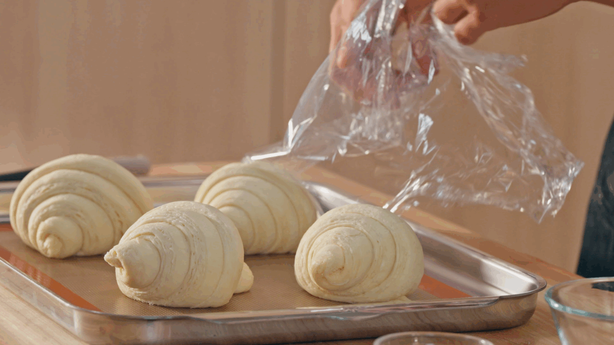 Nick DiGiovanni removing plastic wrap from a tray of proofed croissants. 