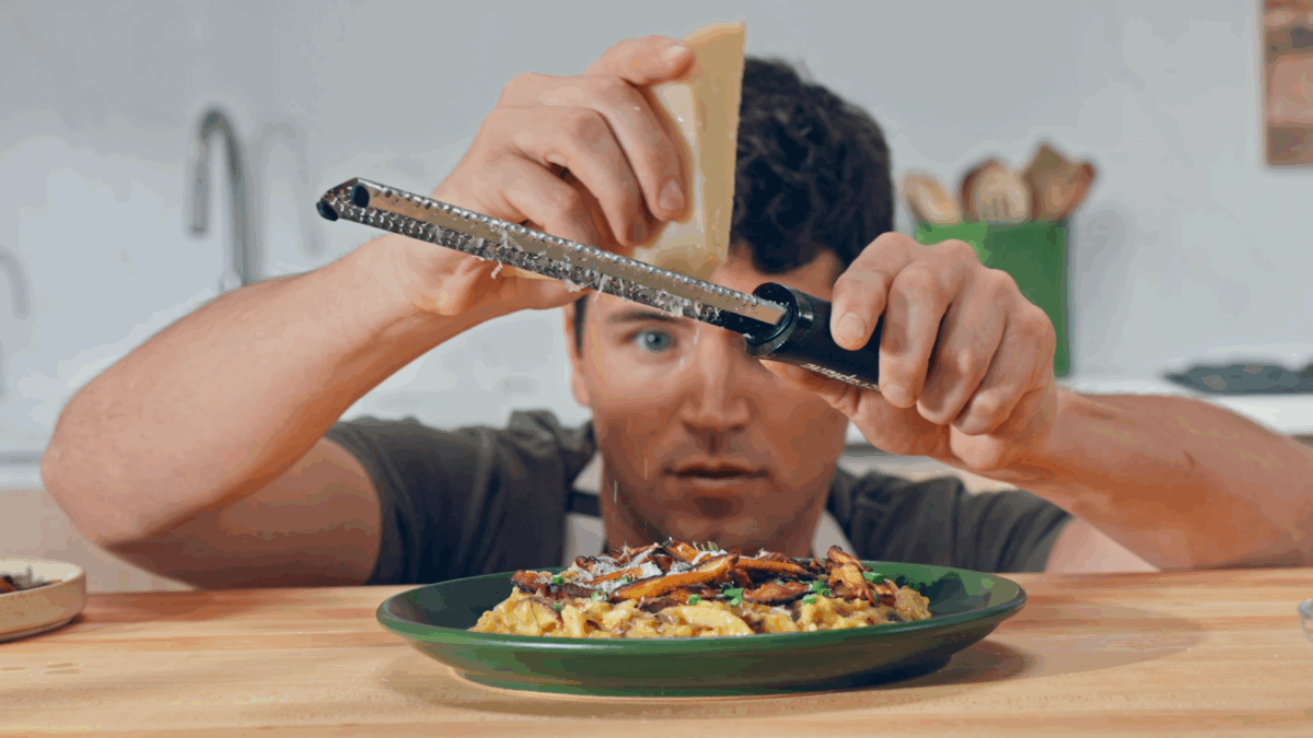 Nick DiGiovanni grating Parmesan cheese over a plate of mushroom risotto.