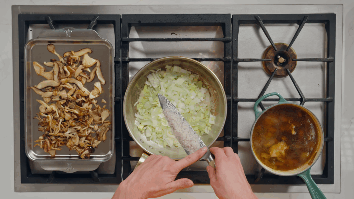 Nick DiGiovanni adding shallots to a pot of leeks on the stovetop.