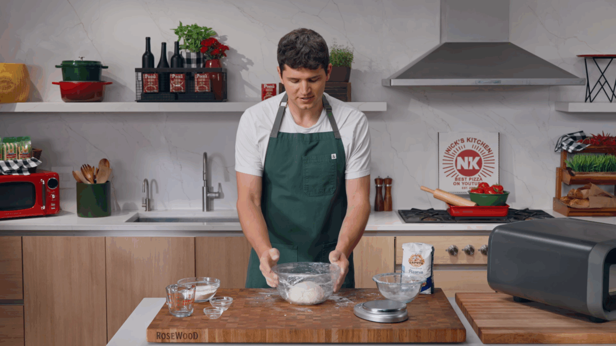 Nick DiGiovanni covering a bowl with a ball of pizza dough with plastic wrap. 