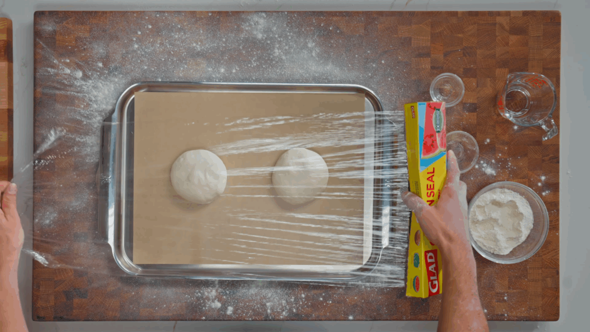 Nick DiGiovanni covering a baking sheet with two balls of pizza dough with plastic wrap. 
