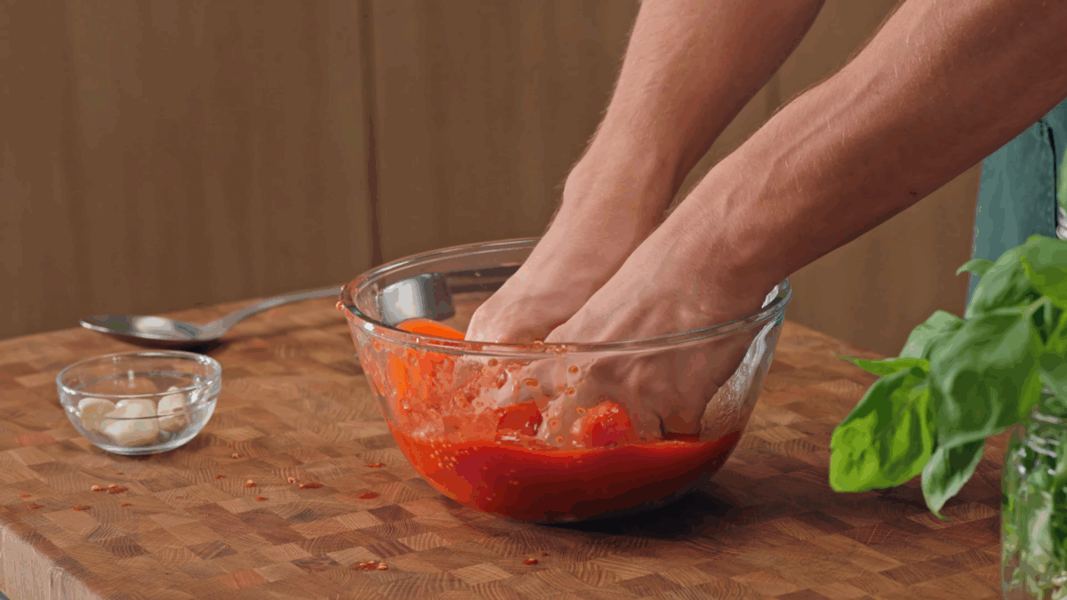 Nick DiGiovanni using his hands to crush tomatoes in a bowl. 