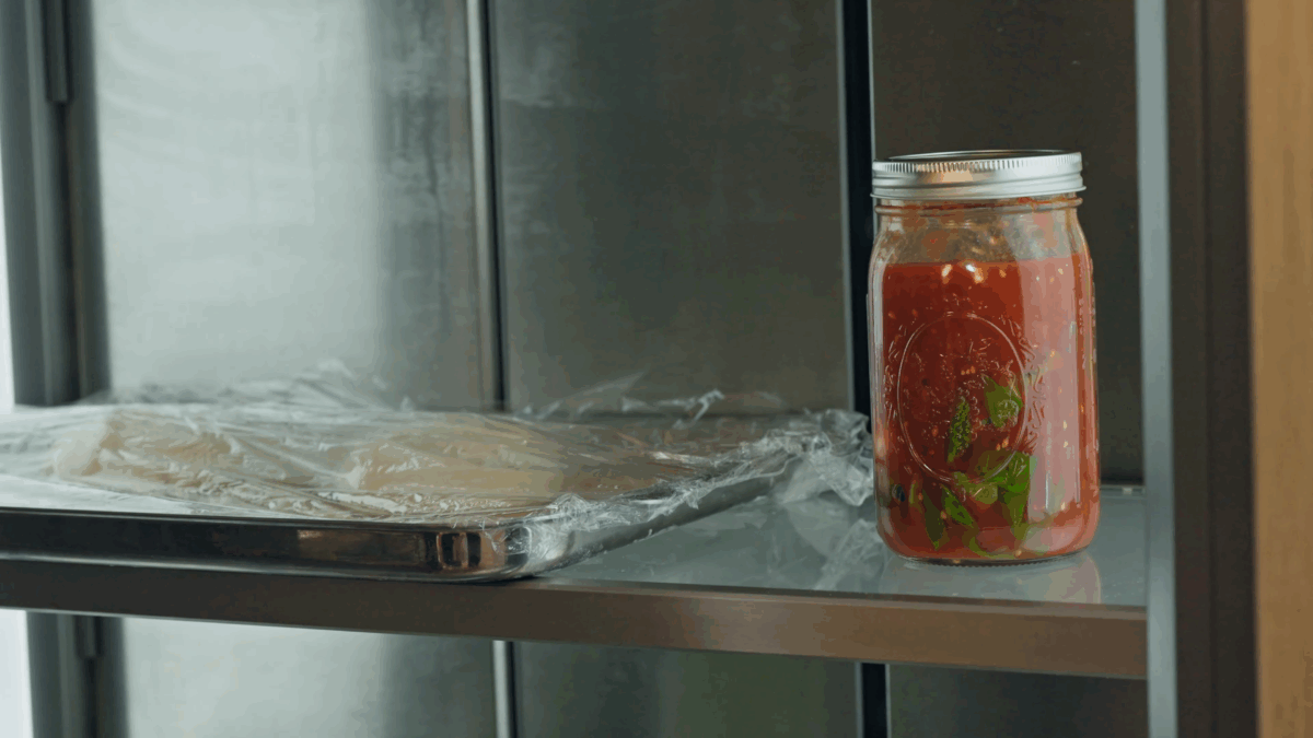 A jar of homemade pizza sauce in a fridge. 