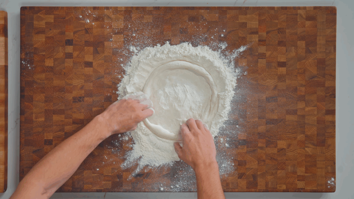 Nick DiGiovanni using two hands to stretch and shape pizza dough.