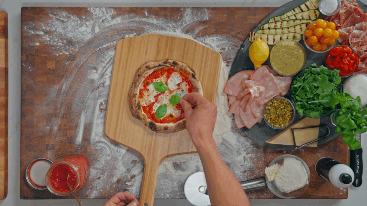 Nick DiGiovanni placing fresh basil on a margherita-style Neapolitan pizza. 