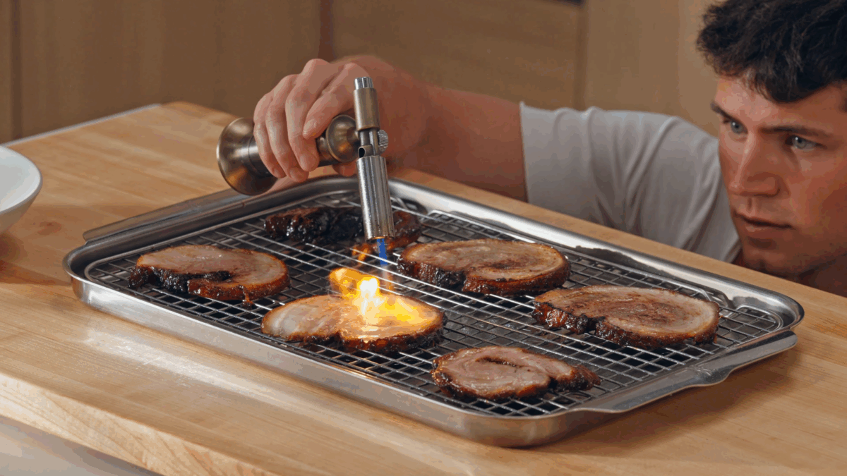 Nick DiGiovanni using a blow torch to sear pork belly pieces.