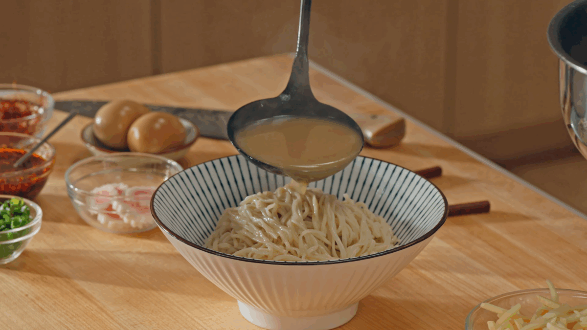 Nick DiGiovanni spooning pork broth over a bowl of ramen noodles. 