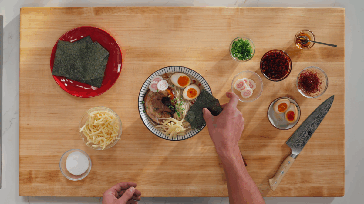Nick DiGiovanni adding toppings to a bowl of mis ramen. 