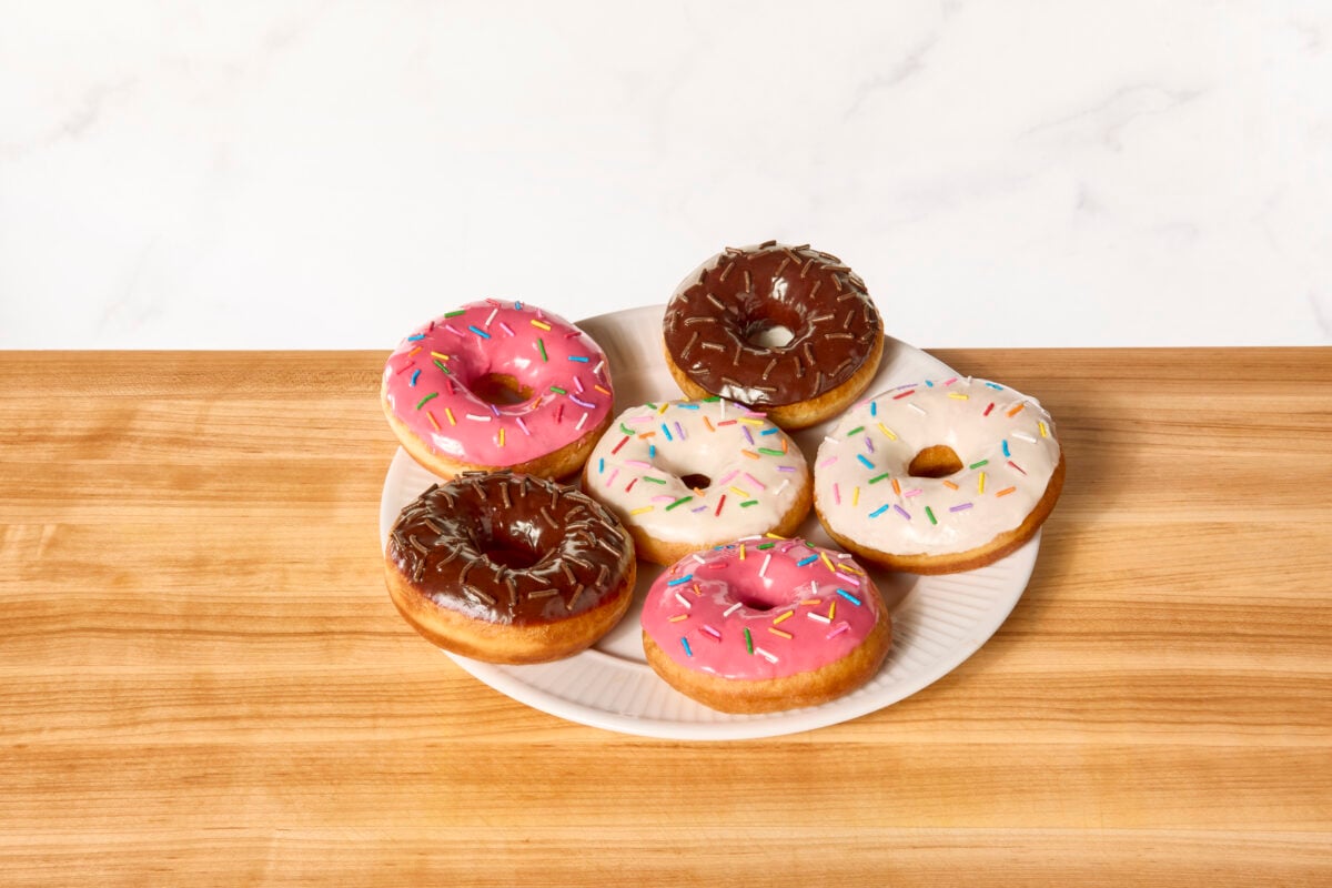 A plate of yeast donuts topped with vanilla glaze, chocolate glaze, strawberry glaze, and sprinkles.