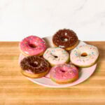 A plate of yeast donuts topped with vanilla glaze, chocolate glaze, strawberry glaze, and sprinkles.