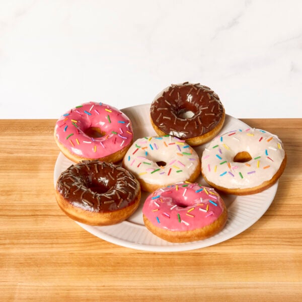 A plate of yeast donuts topped with vanilla glaze, chocolate glaze, strawberry glaze, and sprinkles.