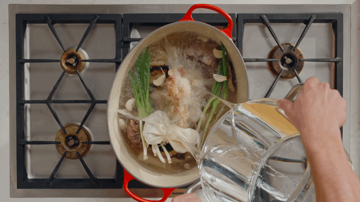 Nick DiGiovanni pouring water over ingredients for beef pho broth in a pot.