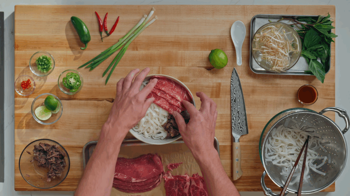 Nick DiGiovanni layering rice noodles and beef in a bowl for Vietnamese beef pho.