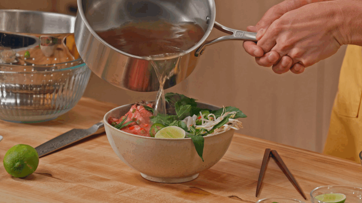 Nick DiGiovanni pouring broth over a bowl of beef pho.