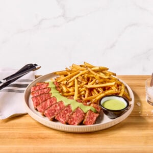 A plate of steak frites with a creamy green herb sauce.