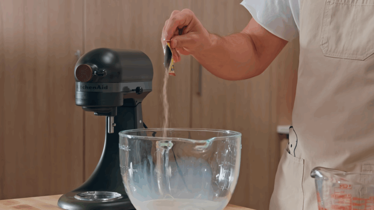 Nick DiGiovanni pouring yeast into the bowl of a stand mixer. 