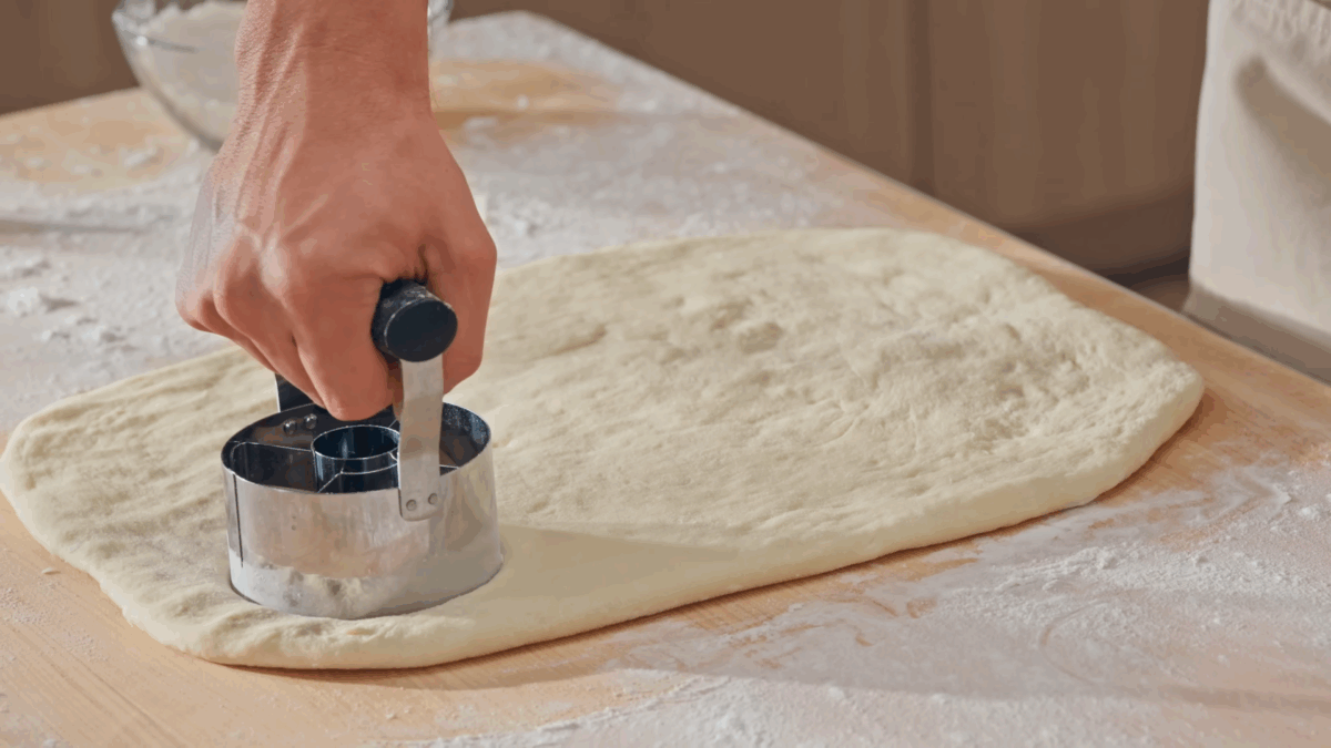 Nick DiGiovanni using a donut cutter to cut donut rings into dough. 
