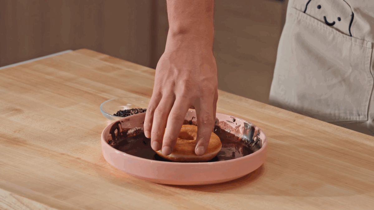 Nick DiGiovanni dipping a yeast donut into a bowl of chocolate frosting. 
