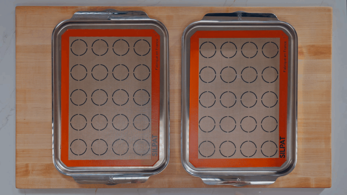 Two baking sheets lined with macaron templates. 