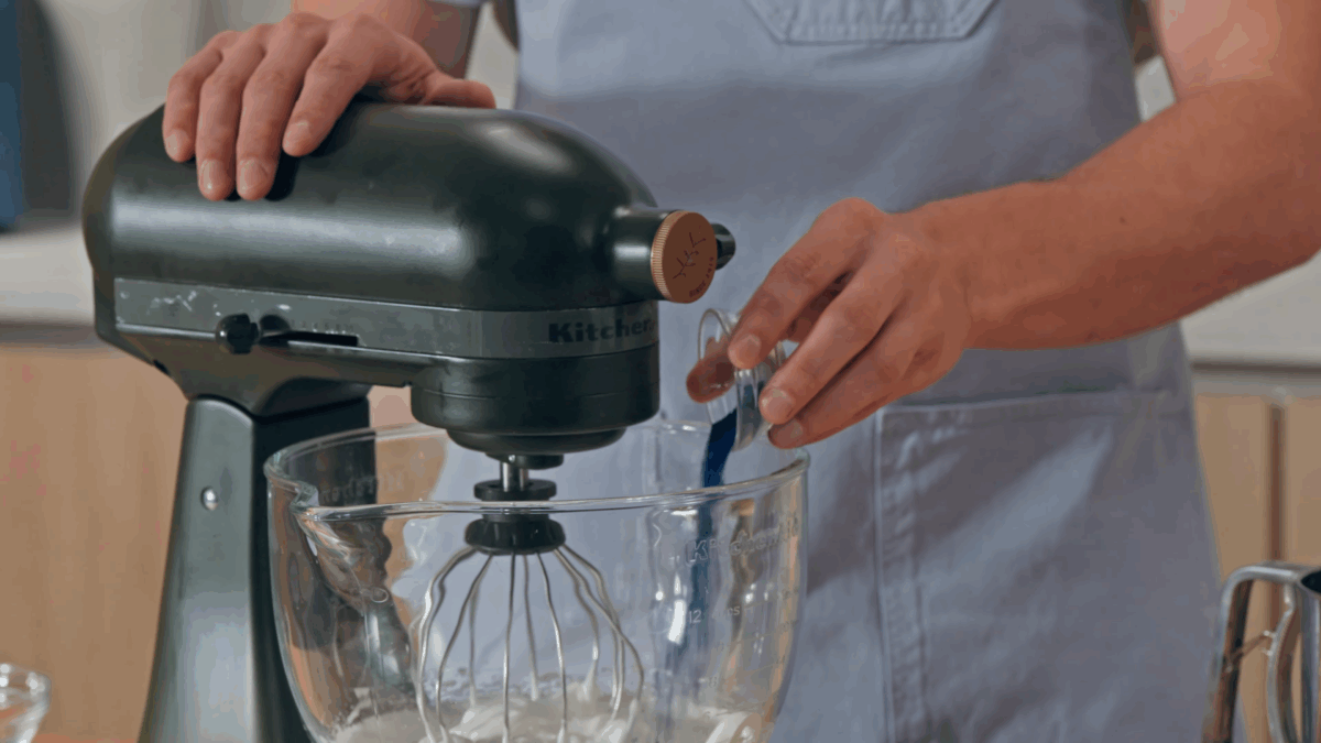 Nick DiGiovanni adding blue powdered food coloring to a stand mixer bowl of meringue. 