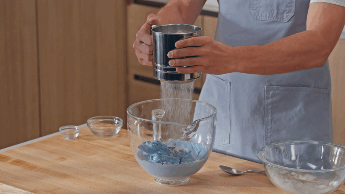 Nick DiGiovanni sifting dry ingredients into a bowl of blue meringue. 