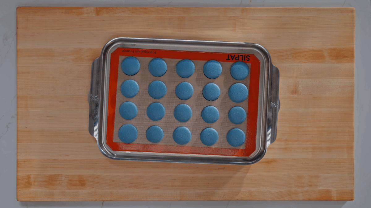 A baking sheet of blue macaron shells. 