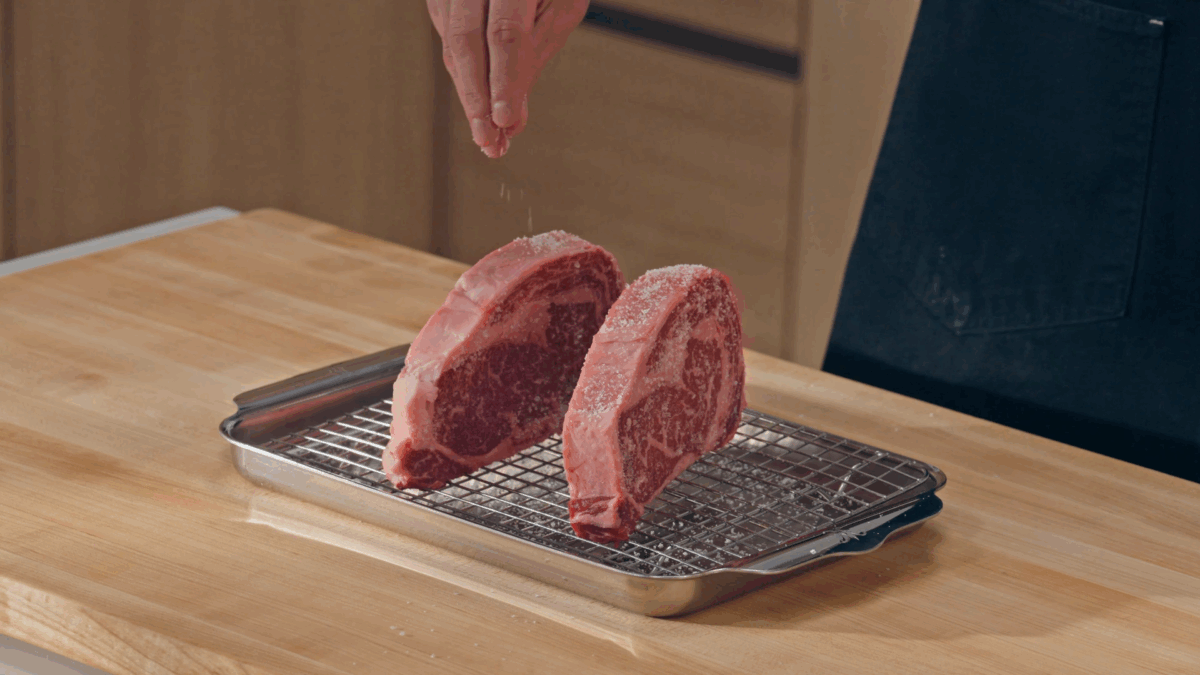 Nick DiGiovanni salting two raw steaks on a wire rack.