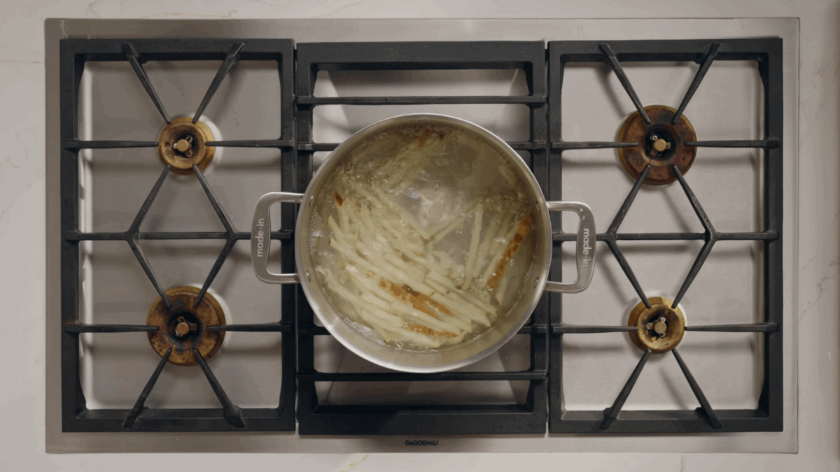 Raw fries soaking in a pot of water on the stovetop.