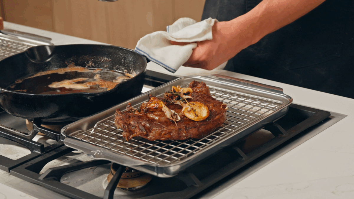 A steak resting on a wire rack.