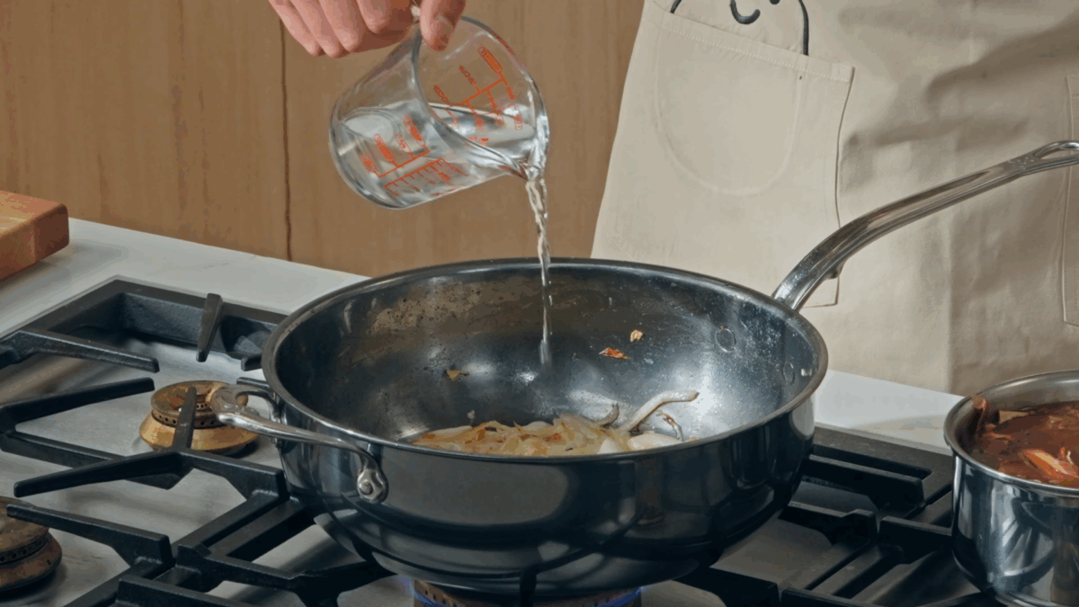 Nick DiGiovanni pouring water into a pan of onions.